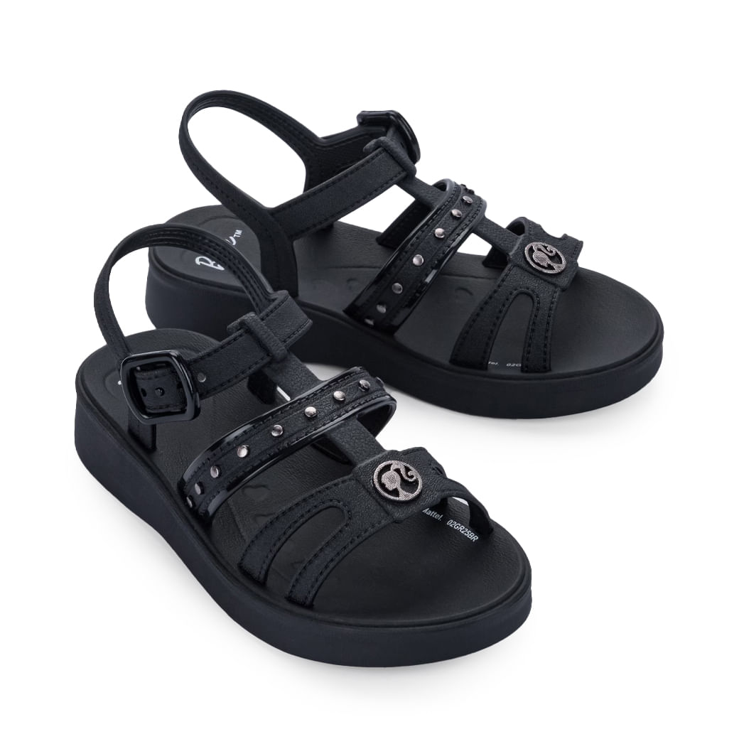 Par de sandálias infantis pretas com tiras e tachas sobre fundo branco.